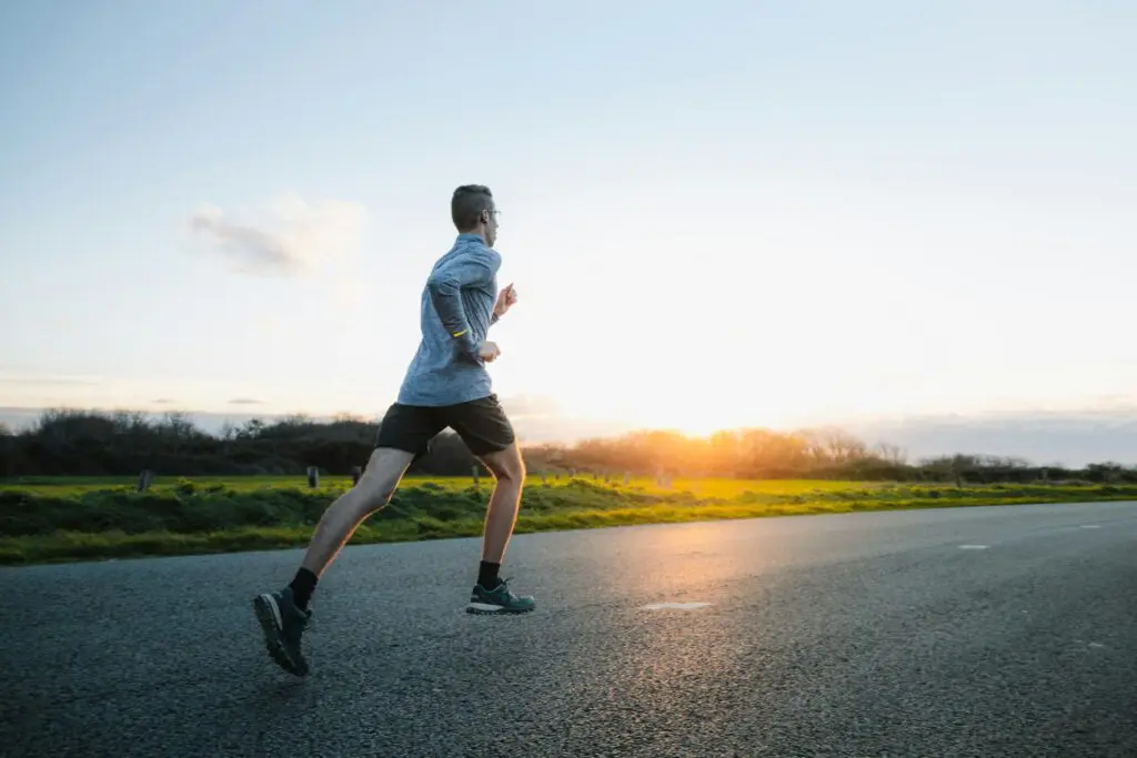 Man running on road during sunrise, dressed in athletic wear.